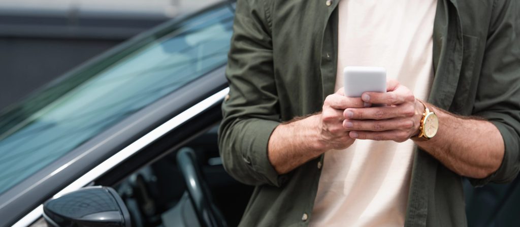 Cropped view of man using smartphone near car