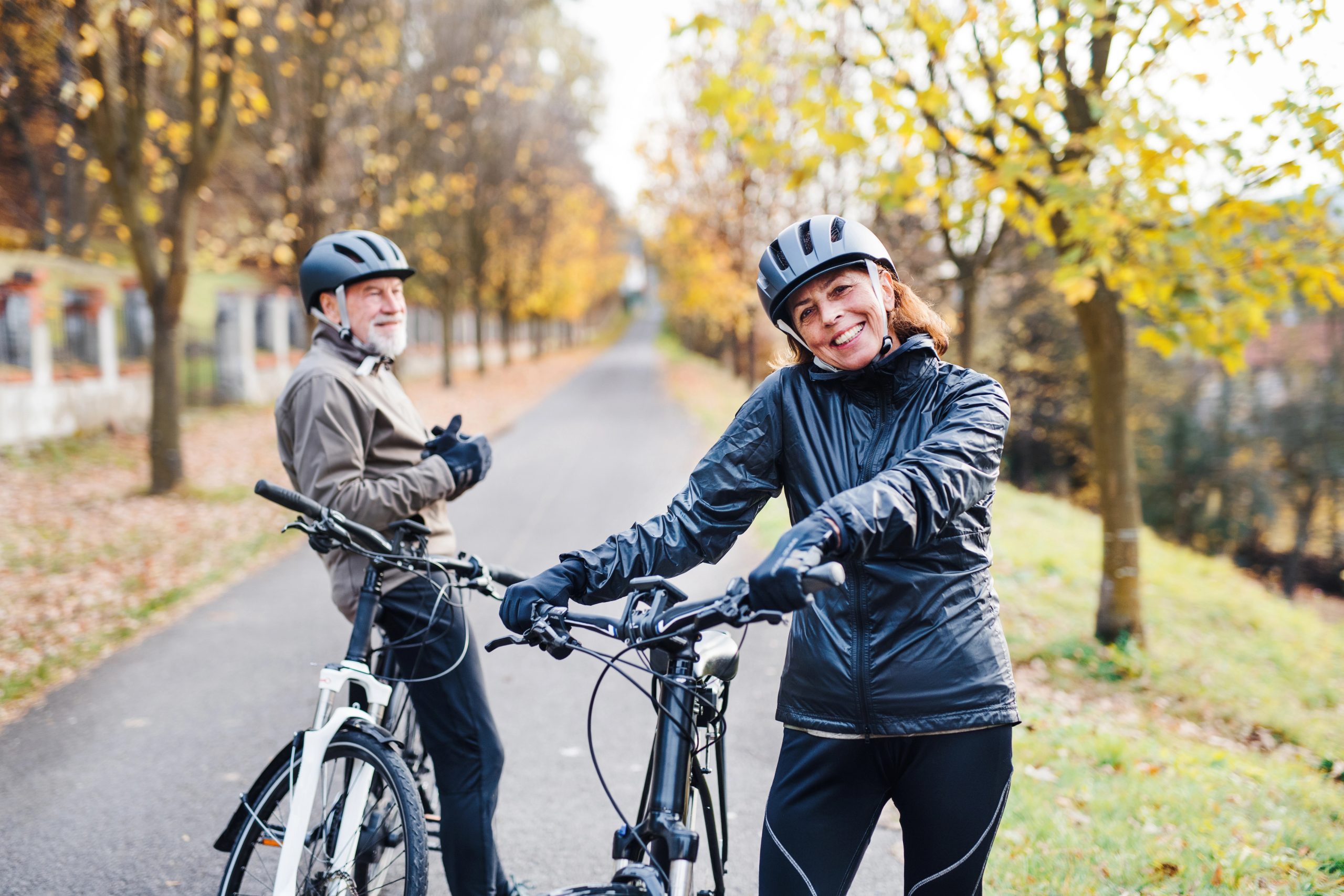 Active senior couple with electrobikes standing outdoors on a road in nature.