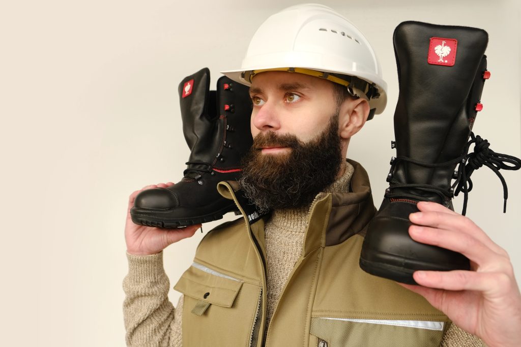 pair black work Strauss boots made leather with reinforced cape, high top in hands of young bearded man, builder in uniform, highest product quality, professional workwear, Frankfurt- November 2022