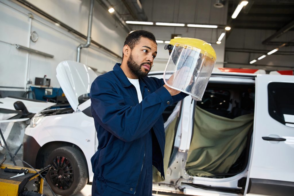 Handsome mechanic focuses on a face shield, showcasing dedication in the vibrant workshop.