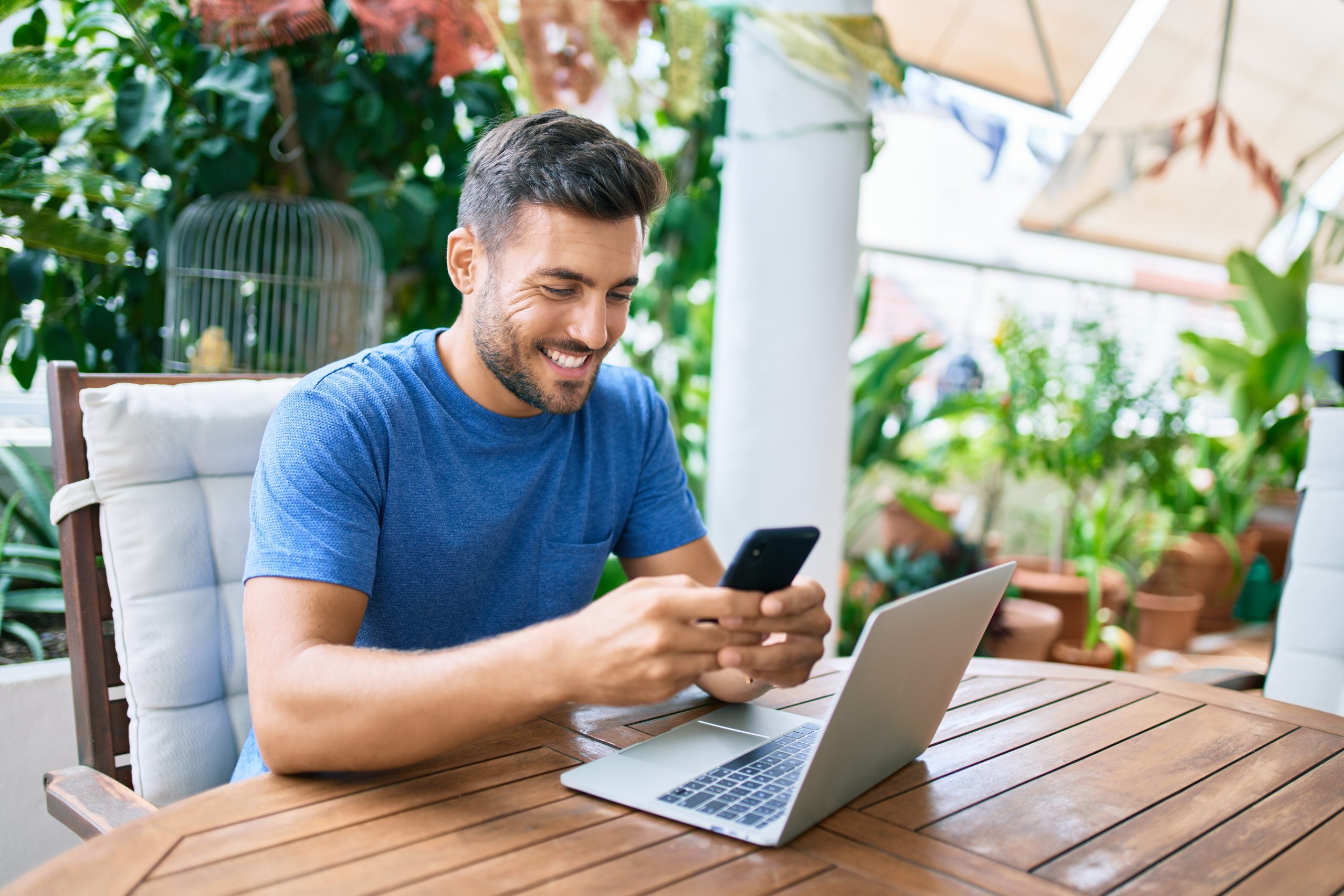 Young hispanic man working using laptop and smartphone at the terrace.